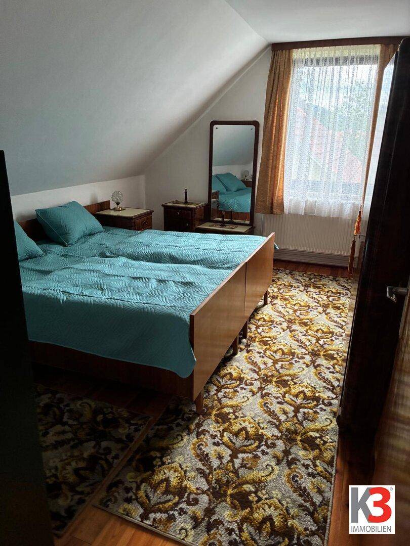 Schlafzimmer mit zwei Einzelbetten, gemustertem Teppich, Holzfußboden und Dachschräge.
