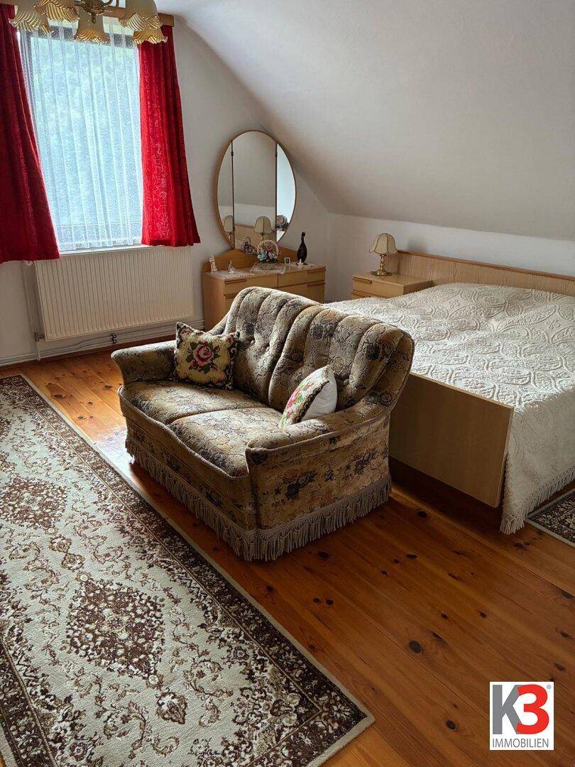 Schlafzimmer mit Doppelbett, kleinem Sofa, Frisiertisch und Holzfußboden unter Dachschräge.