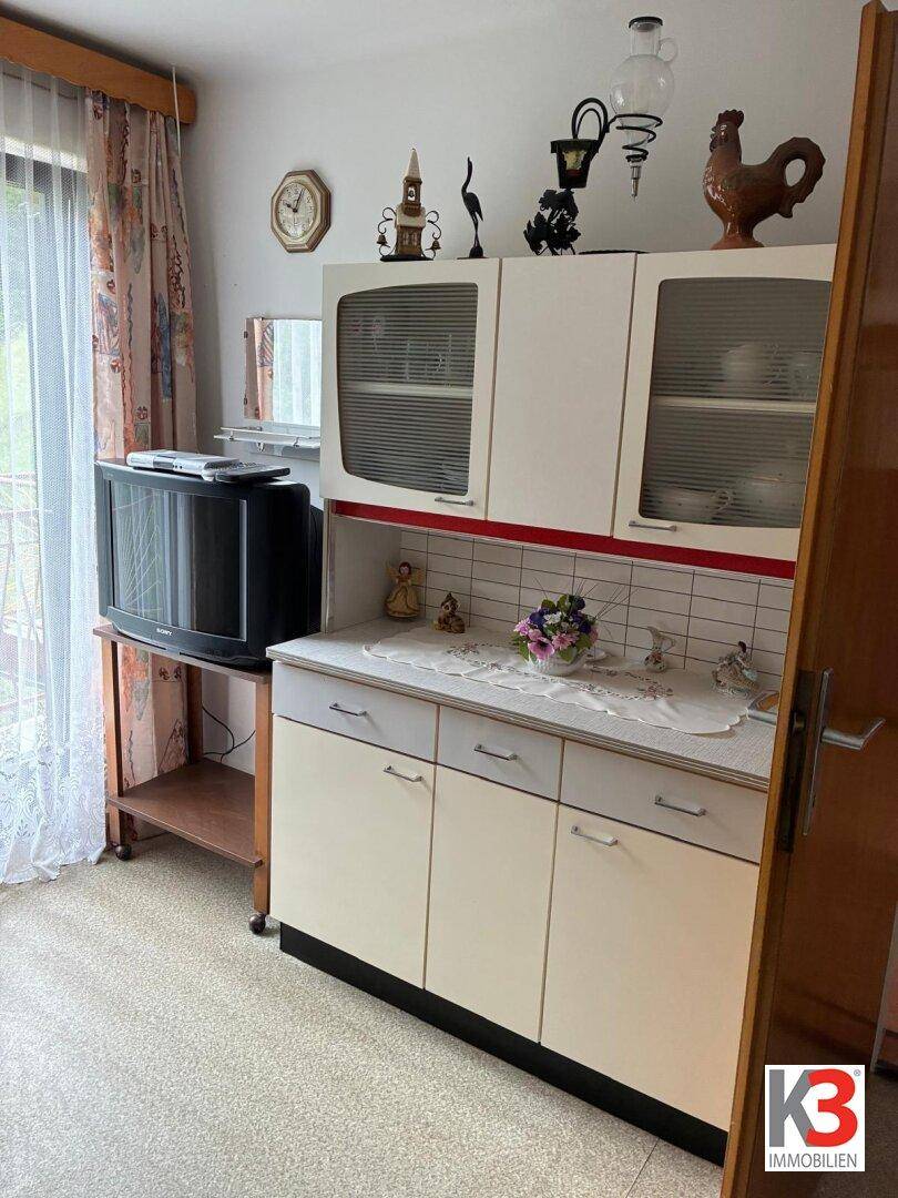 Essbereich oder Mehrzweckraum mit weißem Schrank, Fernseher und Fenster mit Vorhängen.