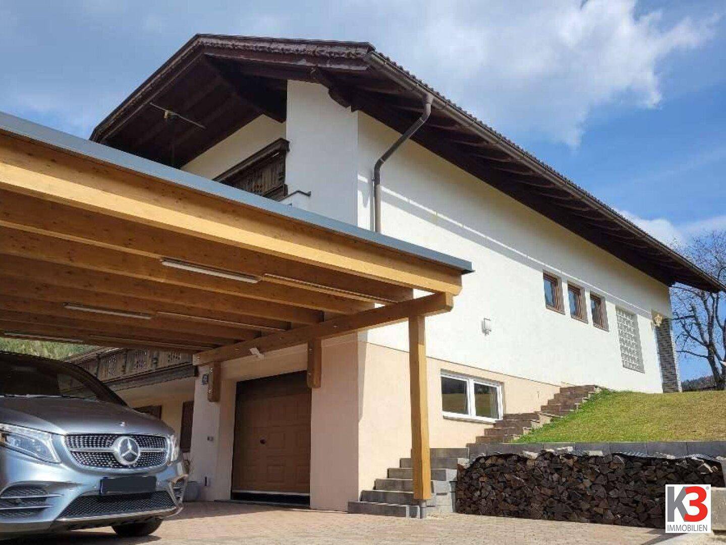 Modernes Einfamilienhaus mit Carport und Garage in alpiner Umgebung.