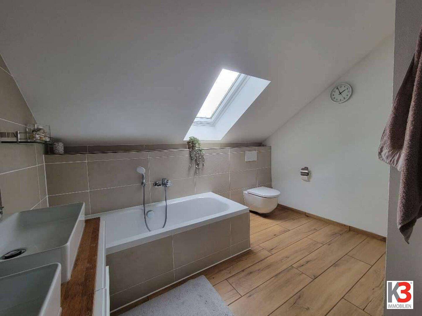 Helles Badezimmer unter dem Dach mit Badewanne, WC und großem Dachfenster.