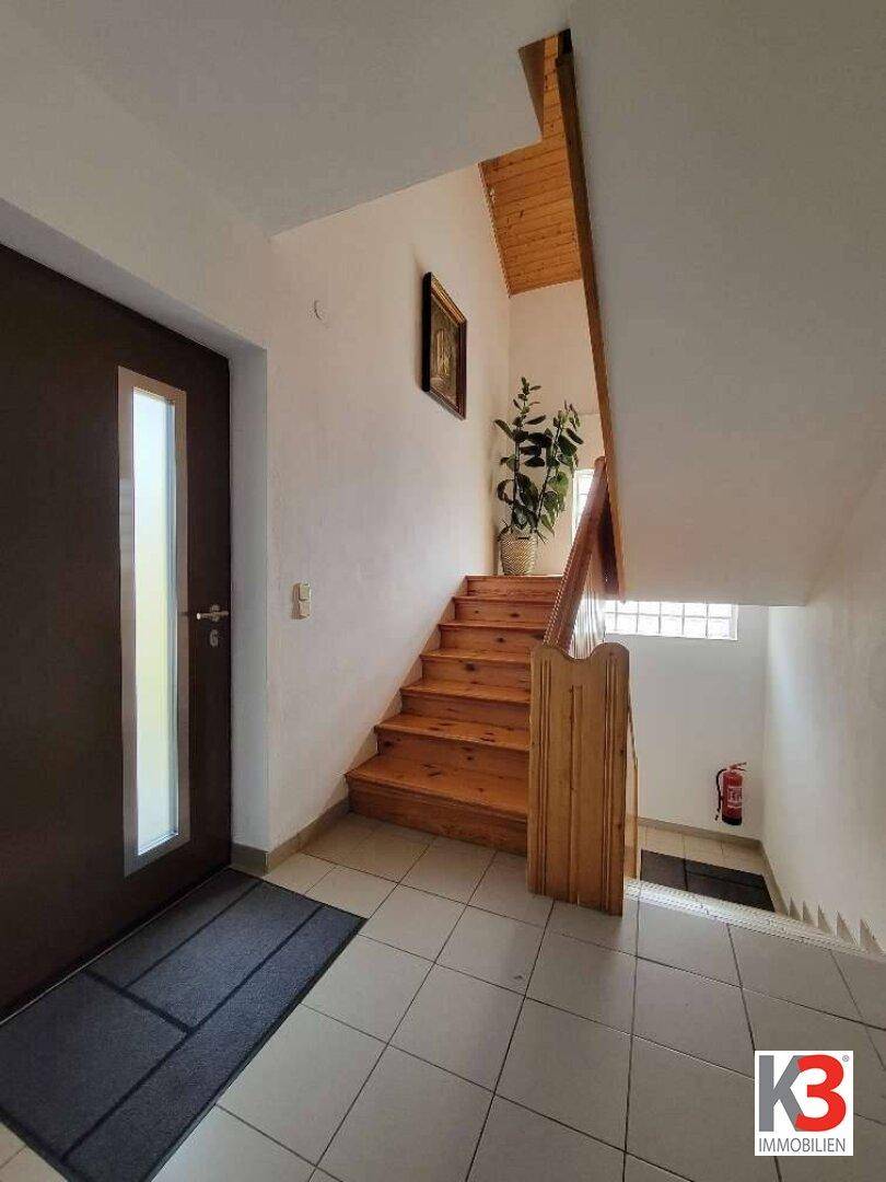Eingangsbereich mit Fliesenboden, Holztreppe und einer Glastür für viel Tageslicht.