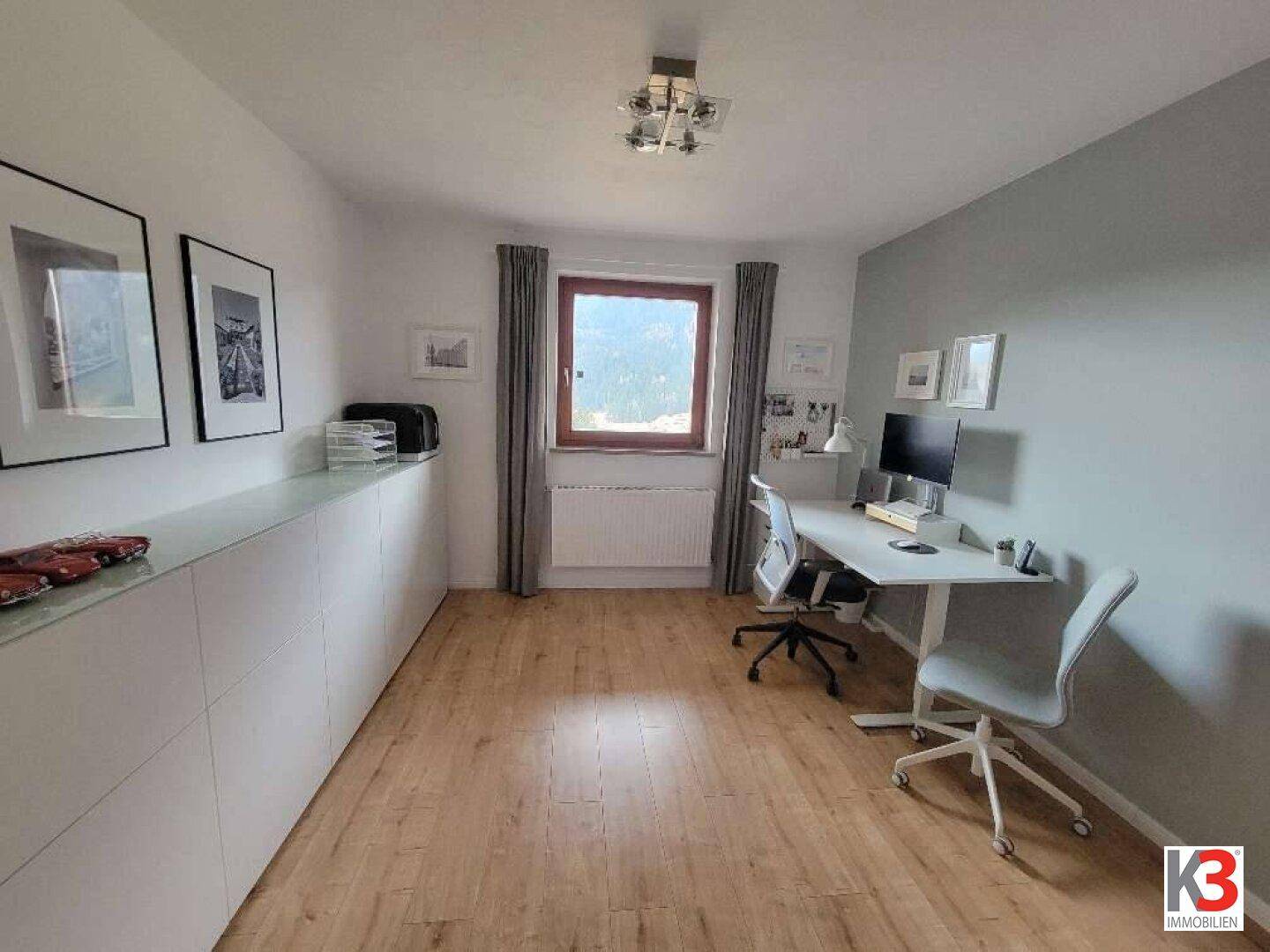 Helles Arbeitszimmer mit Holzfußboden, großem Fenster und modernen Büromöbeln.