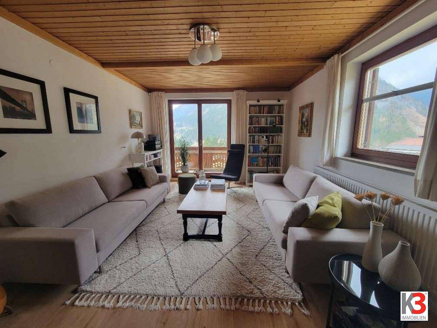 Gemütliches Wohnzimmer mit Holzbalkendecke, bequemen Sofas und Zugang zum Balkon.
