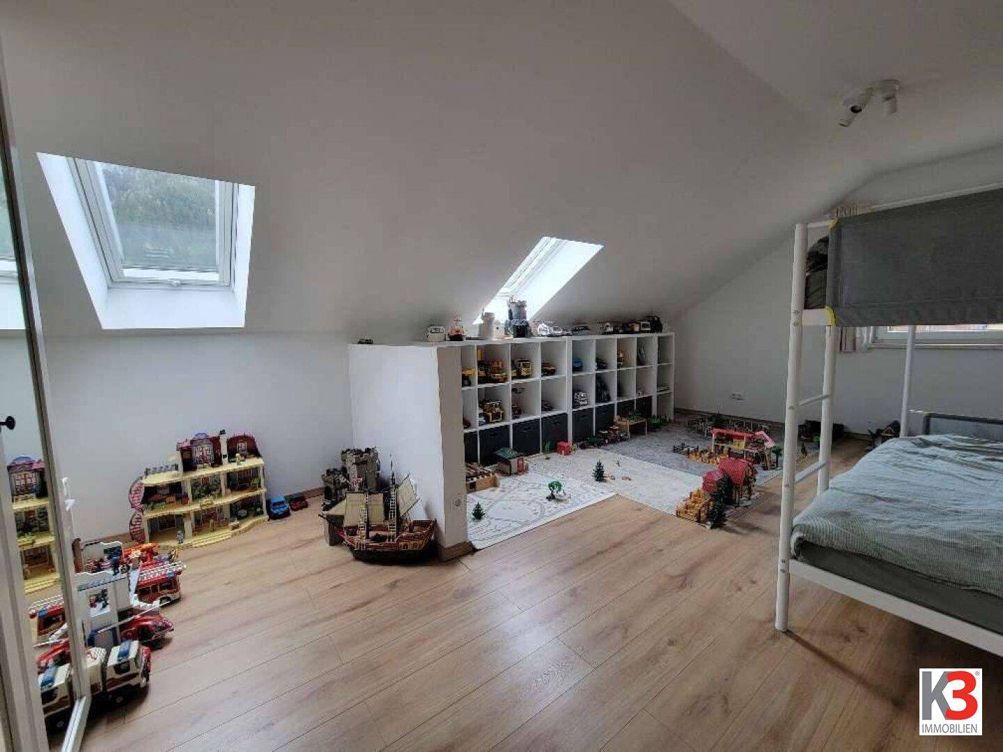 Kinderzimmer mit Dachschräge, Spielzeugregalen und Etagenbett, hell und geräumig.