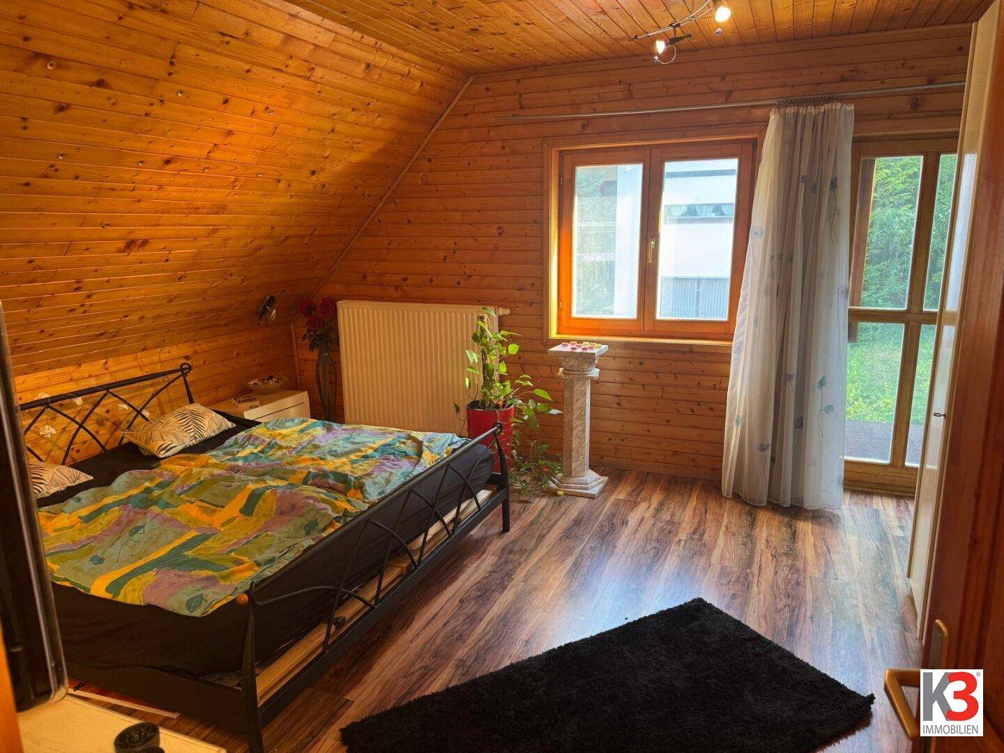 Schlafzimmer mit Holzwänden, Dachschräge und Zugang zu einem kleinen Außenbereich.
