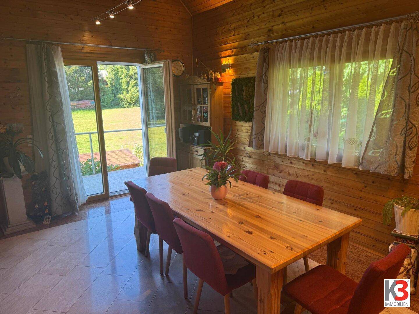 Heller Essbereich mit großem Holztisch, roten Stühlen und direktem Zugang zum Garten.