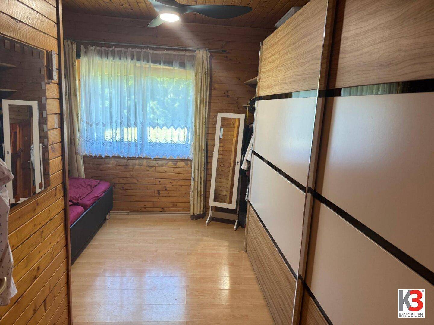 Schlafzimmer mit Holzvertäfelung, hellem Holzboden und großem Kleiderschrank.