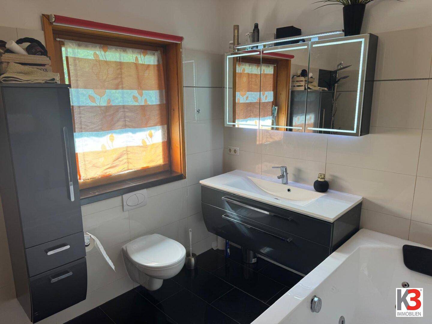 Modernes Badezimmer mit Whirlpool, Wand-WC und beleuchtetem Spiegelschrank.