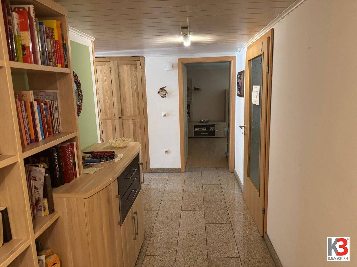 Heller Flur mit Fliesenboden, Bücherregal und Holztüren.