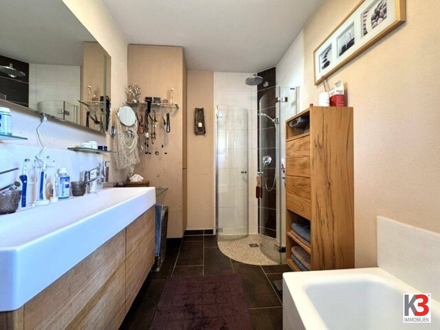 Modernes Badezimmer mit Doppelwaschbecken, großer Dusche und dunklen Fliesen.