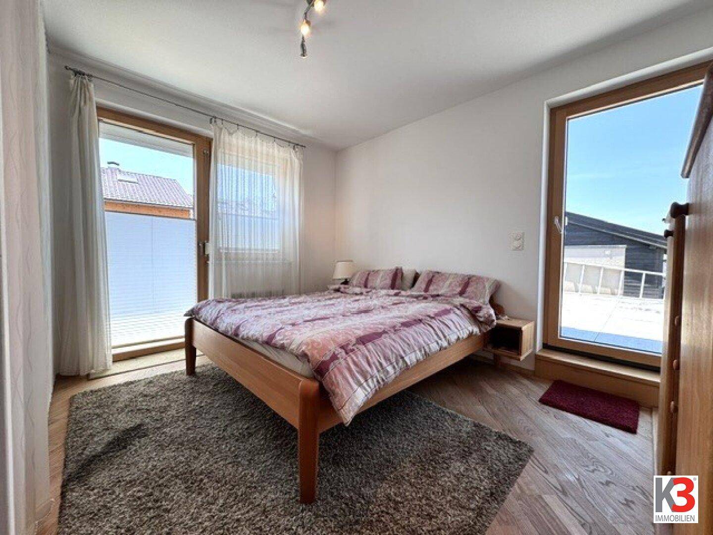 Schlafzimmer mit Holzboden, Doppelbett und Zugang zu einem Balkon oder Terrasse.