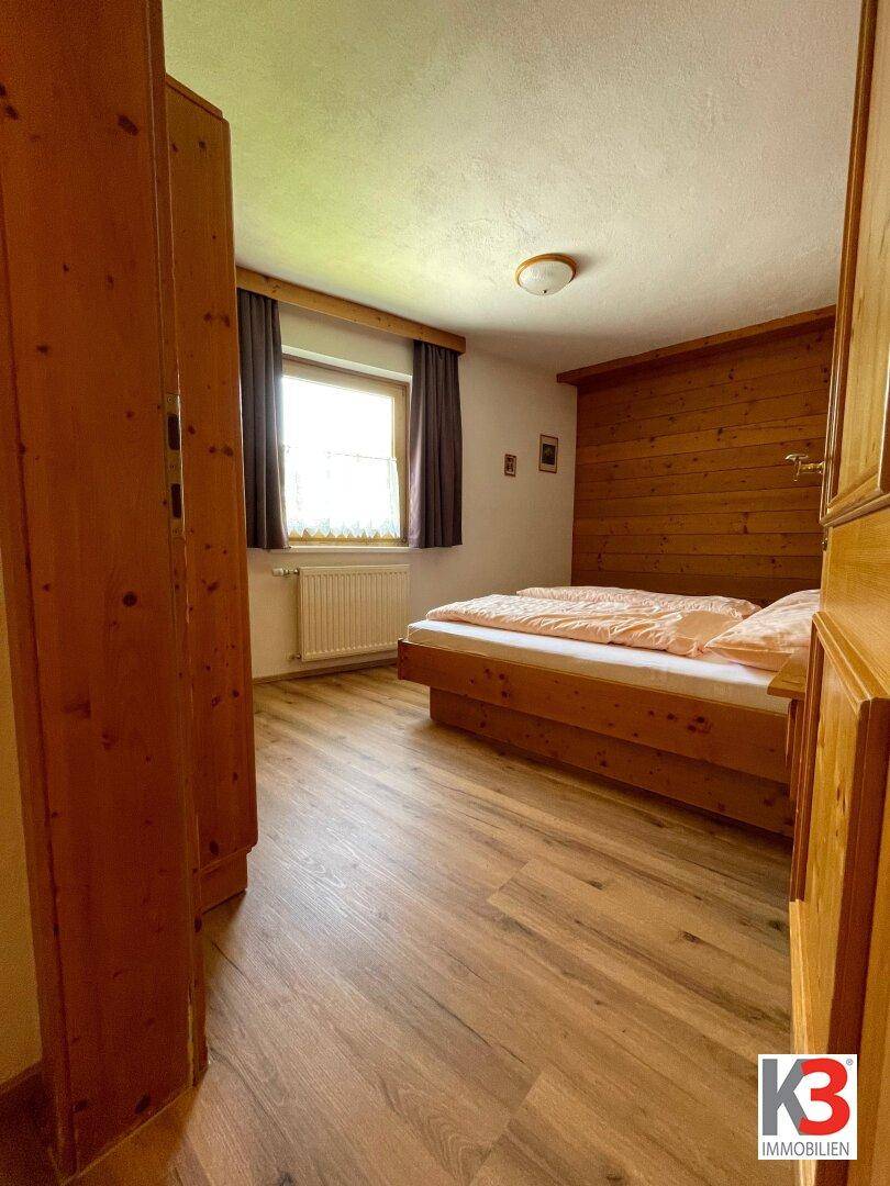 Gemütliches Schlafzimmer mit Holzbett, Laminatboden und einem Fenster mit Blick ins Grüne.