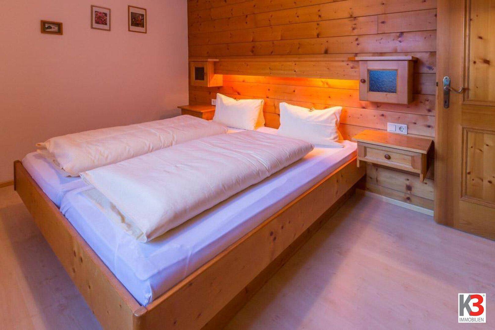 Schlafzimmer mit Doppelbett, Holzvertäfelung an der Wand und integrierter Beleuchtung.
