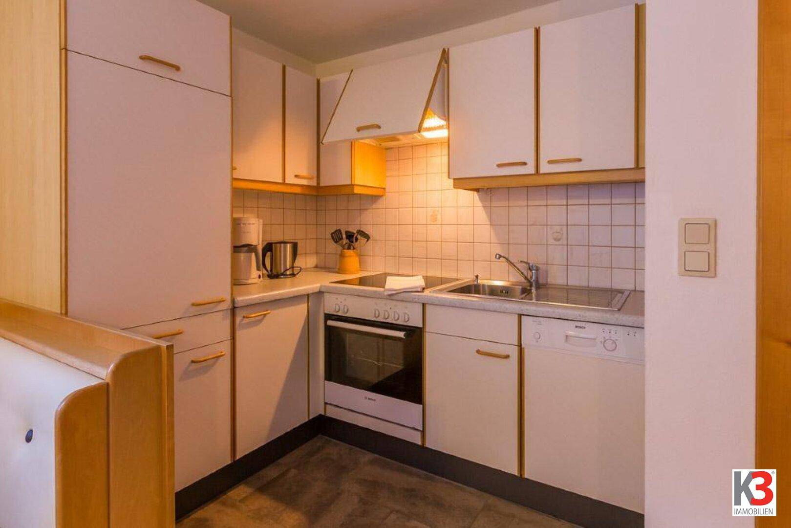 Funktionale Küche mit weißen Schränken, Fliesenrückwand und integrierten Geräten.