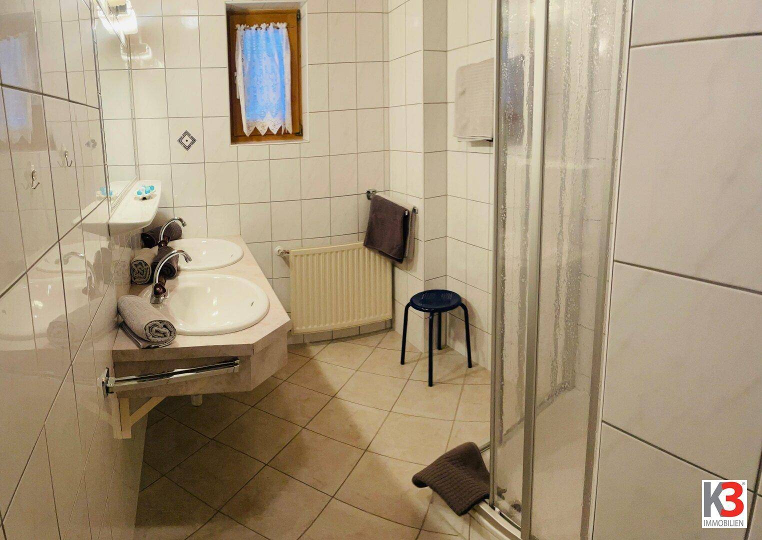 Badezimmer mit zwei Waschbecken, Duschkabine und einem Fenster für Tageslicht.