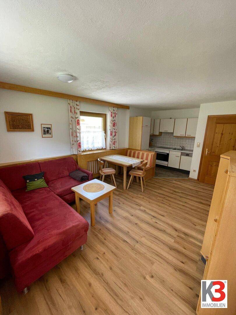 Offener Wohnbereich mit rotem Sofa, Essbereich und integrierter Küchenzeile.
