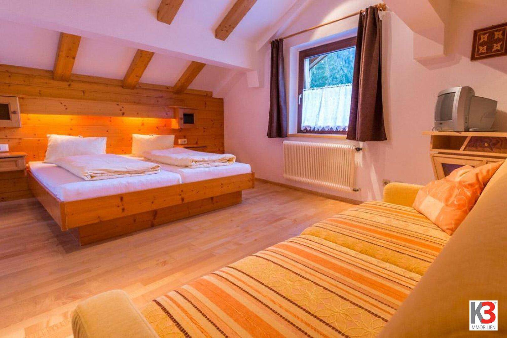 Schlafzimmer im Dachgeschoss mit Holzbalken, Doppelbett und einem Sofa.