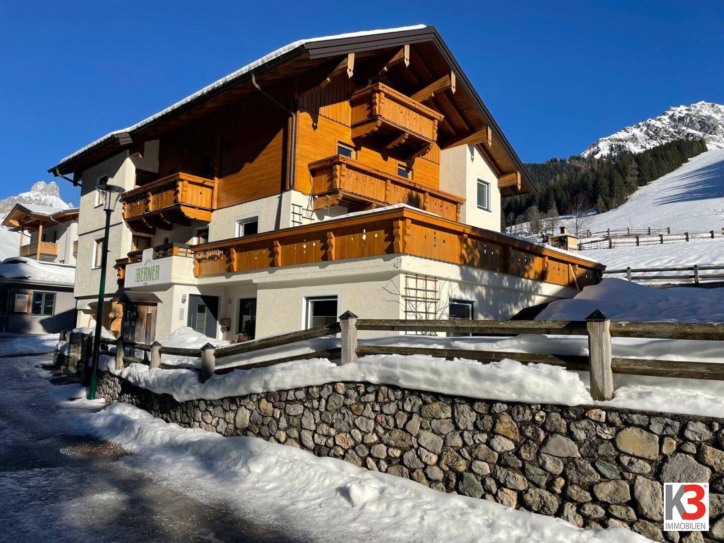 Gebäude in alpiner Winterlandschaft mit Schnee und Bergen im Hintergrund.