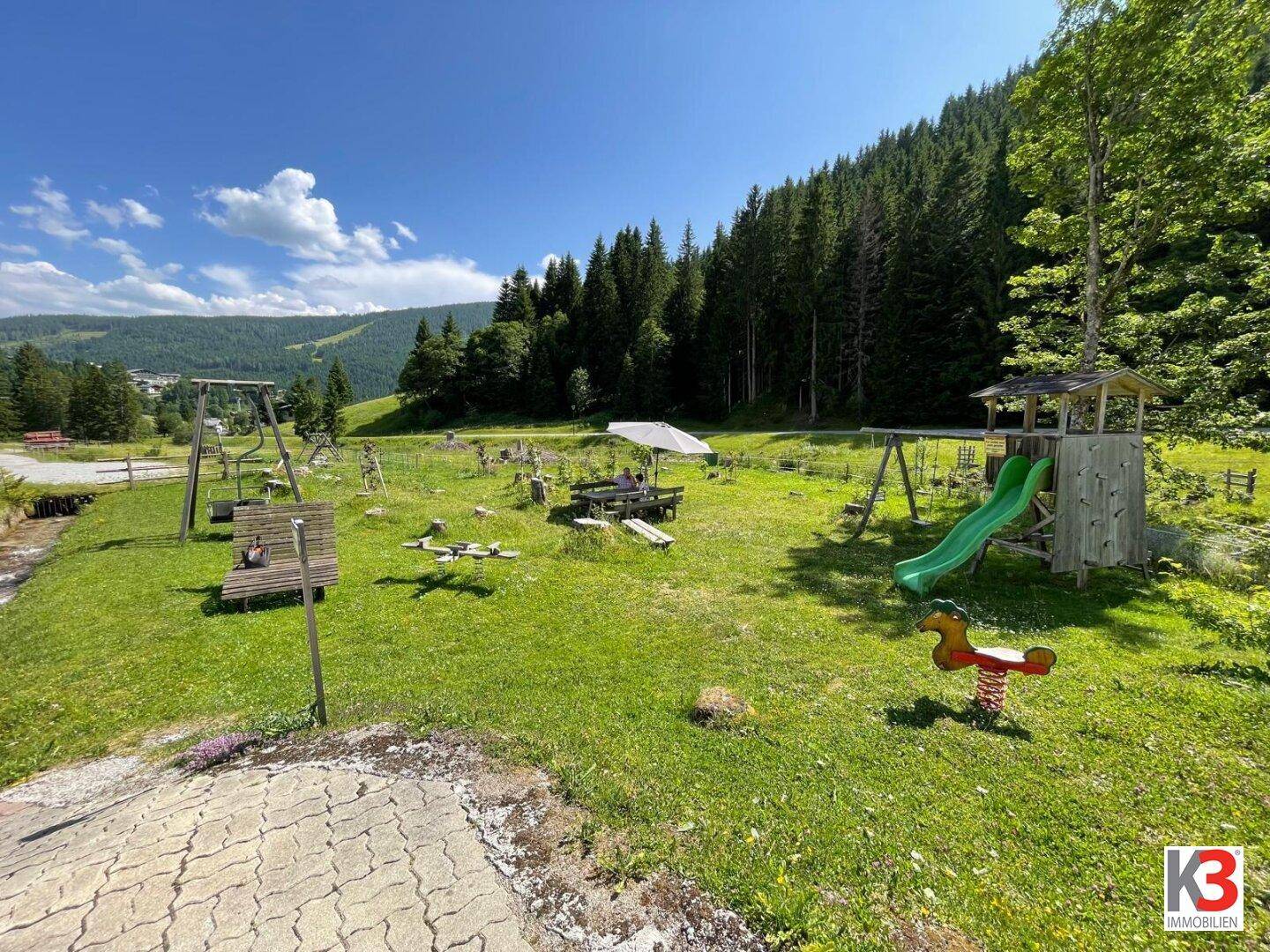 Kinderspielplatz mit Schaukeln und Rutsche in einer weitläufigen grünen Landschaft.