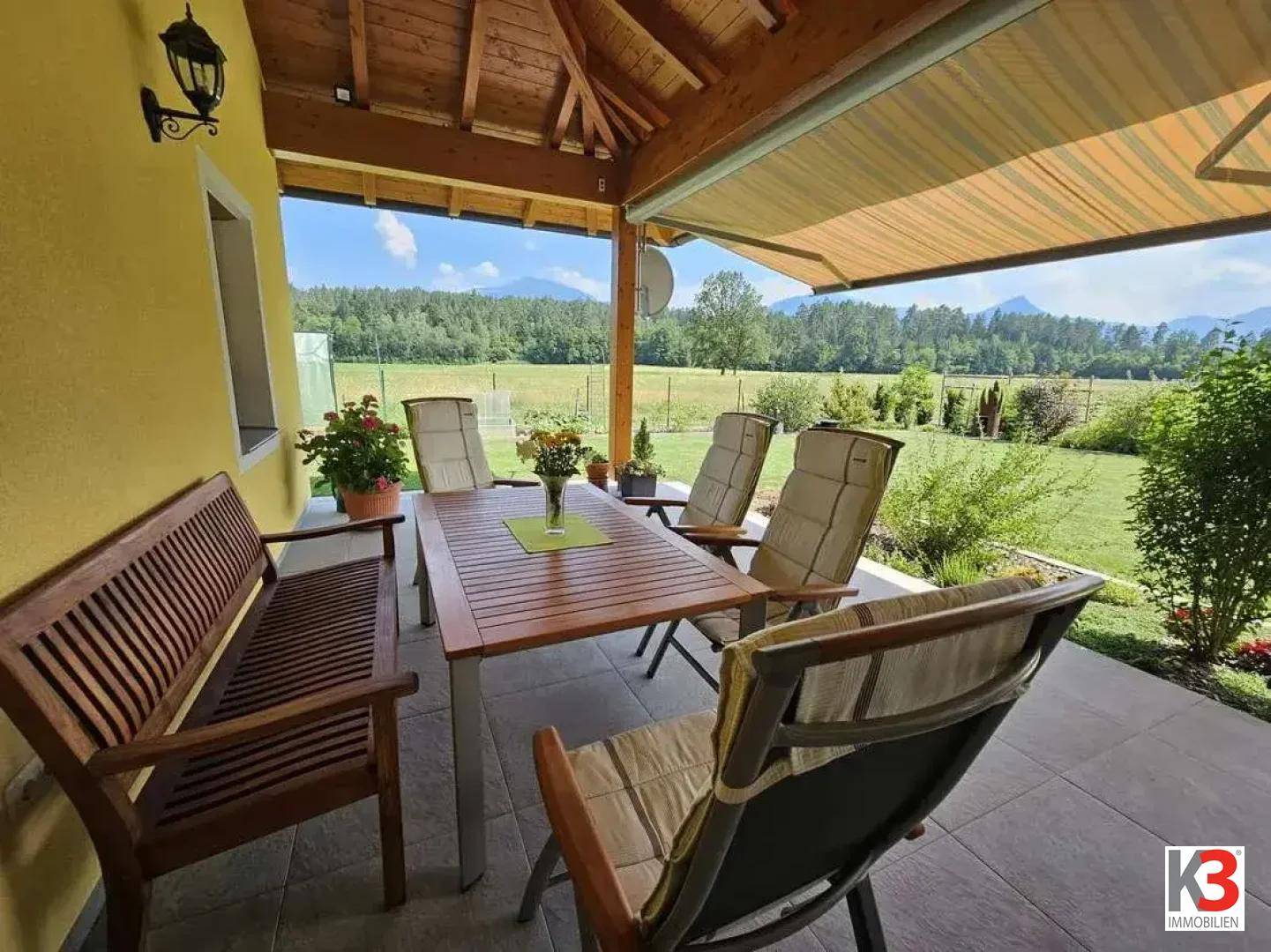 Gemütliche überdachte Terrasse mit Gartenmöbeln und weitem Blick auf die Landschaft und Berge.