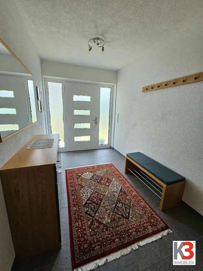 Heller Eingangsbereich mit moderner Haustür, Schuhbank und Spiegel.