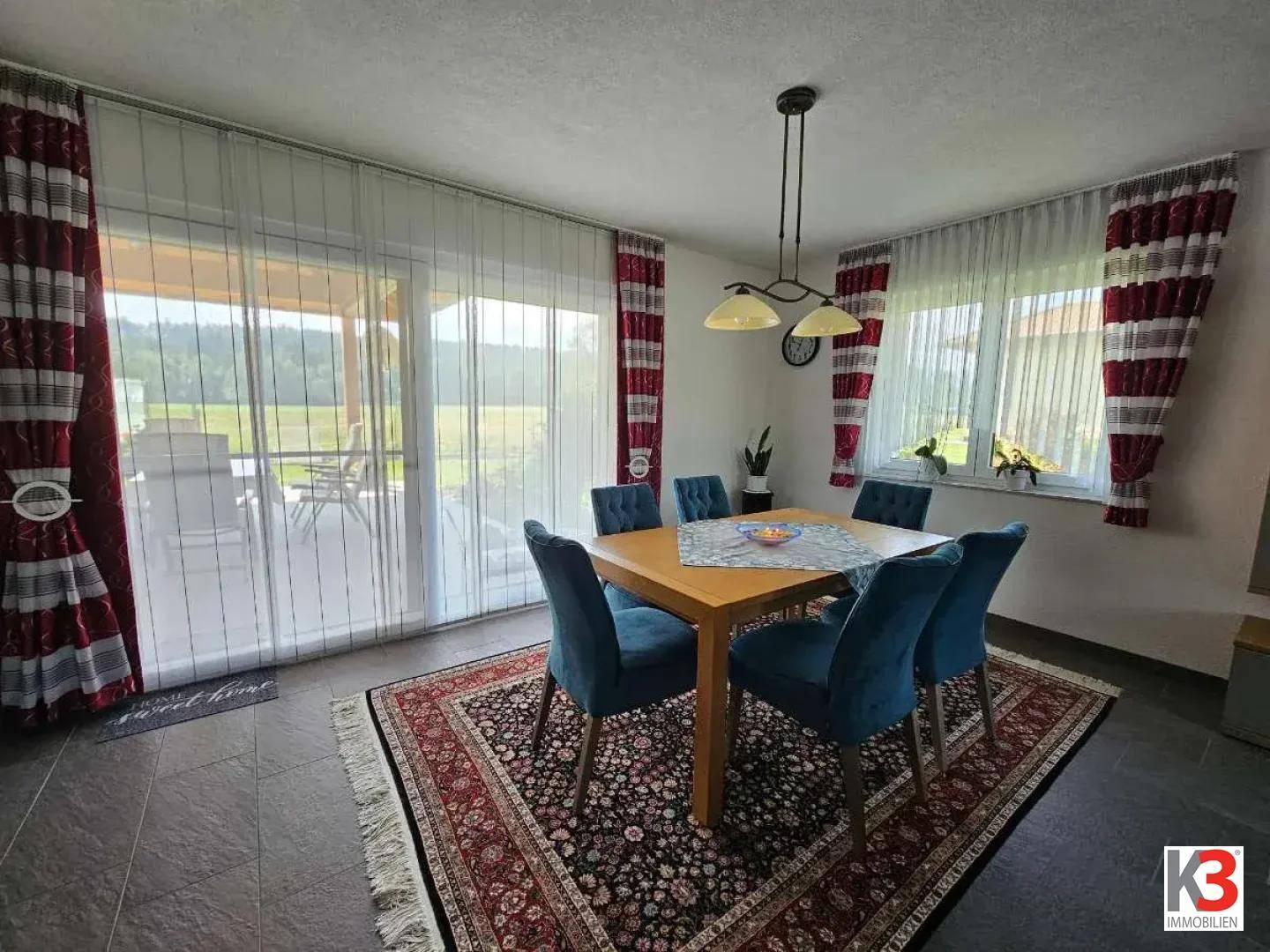 Esszimmer mit Holztisch, blauen Stühlen und Zugang zur Terrasse mit Blick ins Grüne.