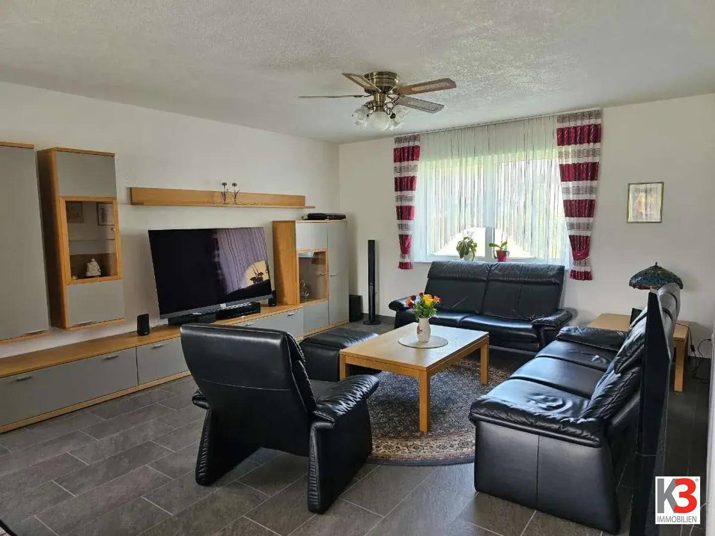 Gemütliches Wohnzimmer mit schwarzen Ledersofas, Couchtisch und Deckenventilator.