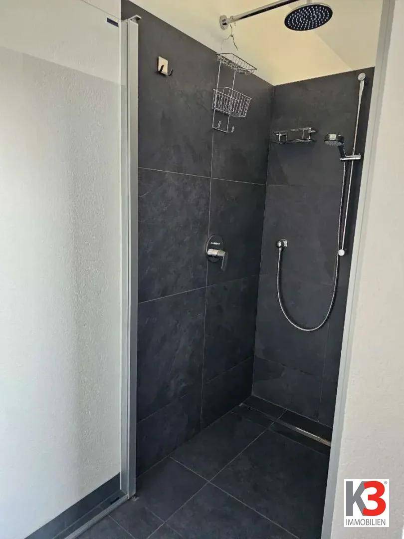 Moderne Duschkabine mit dunklen Fliesen und Regendusche.