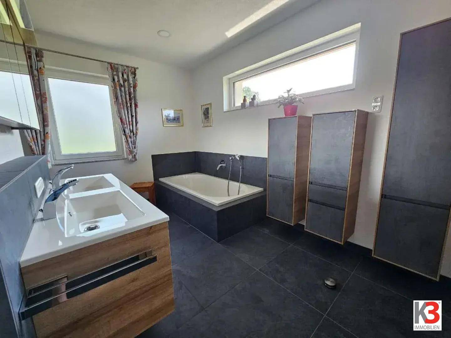 Modernes Badezimmer mit Doppelwaschbecken, eingebauter Badewanne und zwei Fenstern.