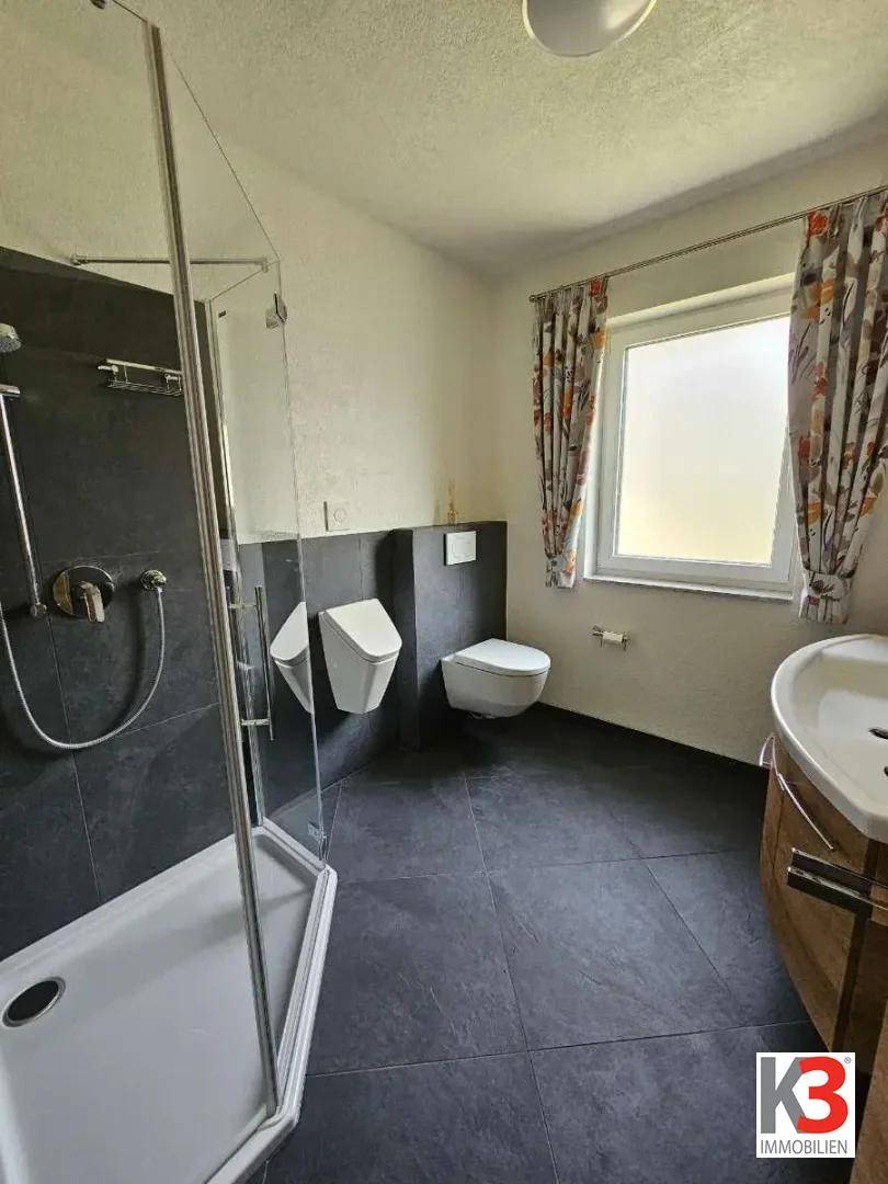 Badezimmer mit Duschkabine, Toilette, Waschbecken und Fenster.