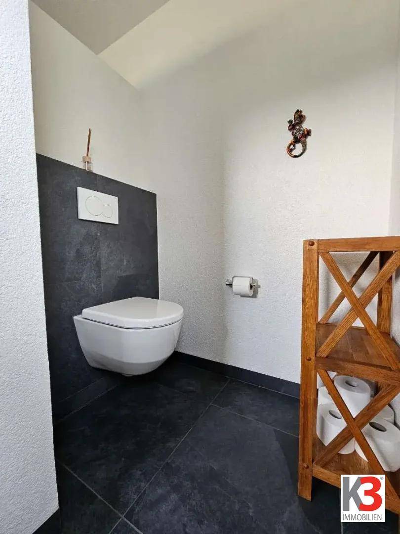 Separates Gäste-WC mit wandhängender Toilette und kleinem Holzregal.