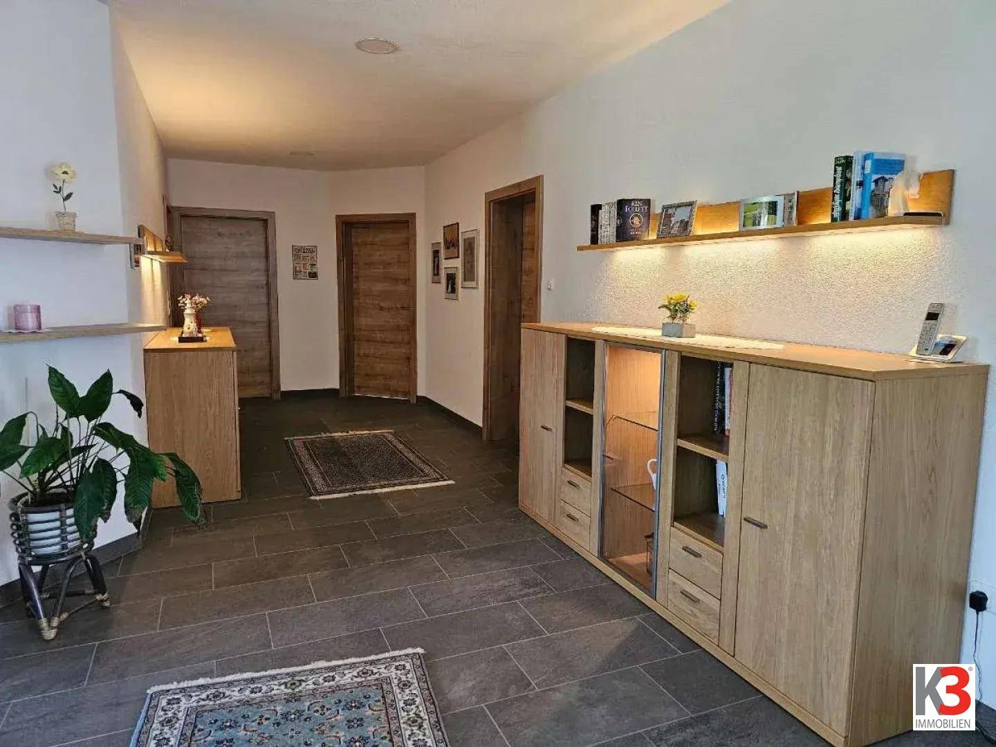 Geräumiger Flur mit Holzmöbeln, beleuchteten Regalen und mehreren Türen.