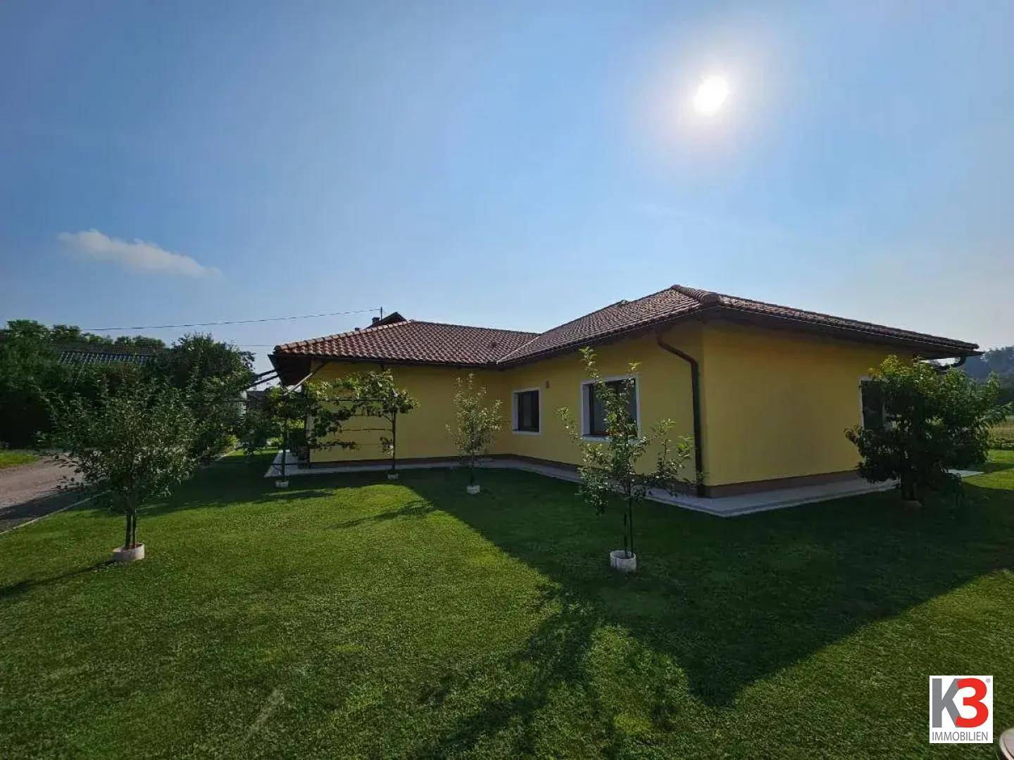 Außenansicht des Hauses mit weitläufiger Rasenfläche unter strahlendem Sonnenschein.