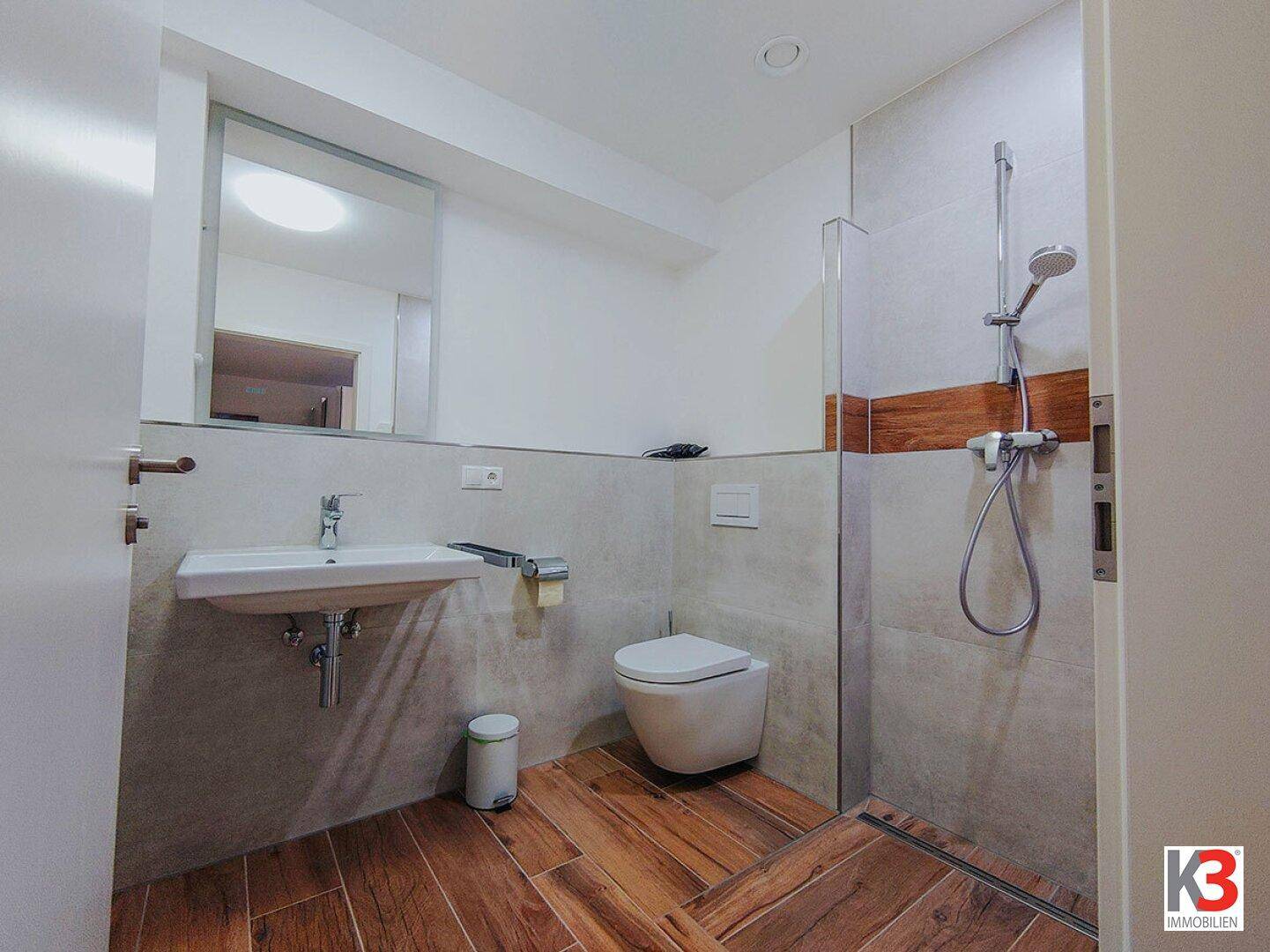 Modernes Badezimmer mit ebenerdiger Dusche, wandhängendem WC und Einzelwaschbecken.
