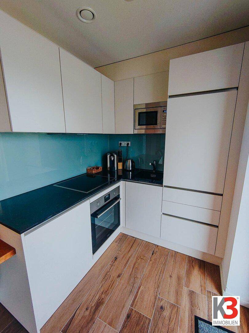 Moderne Einbauküche mit weißen Fronten, Induktionskochfeld und blauer Rückwand.