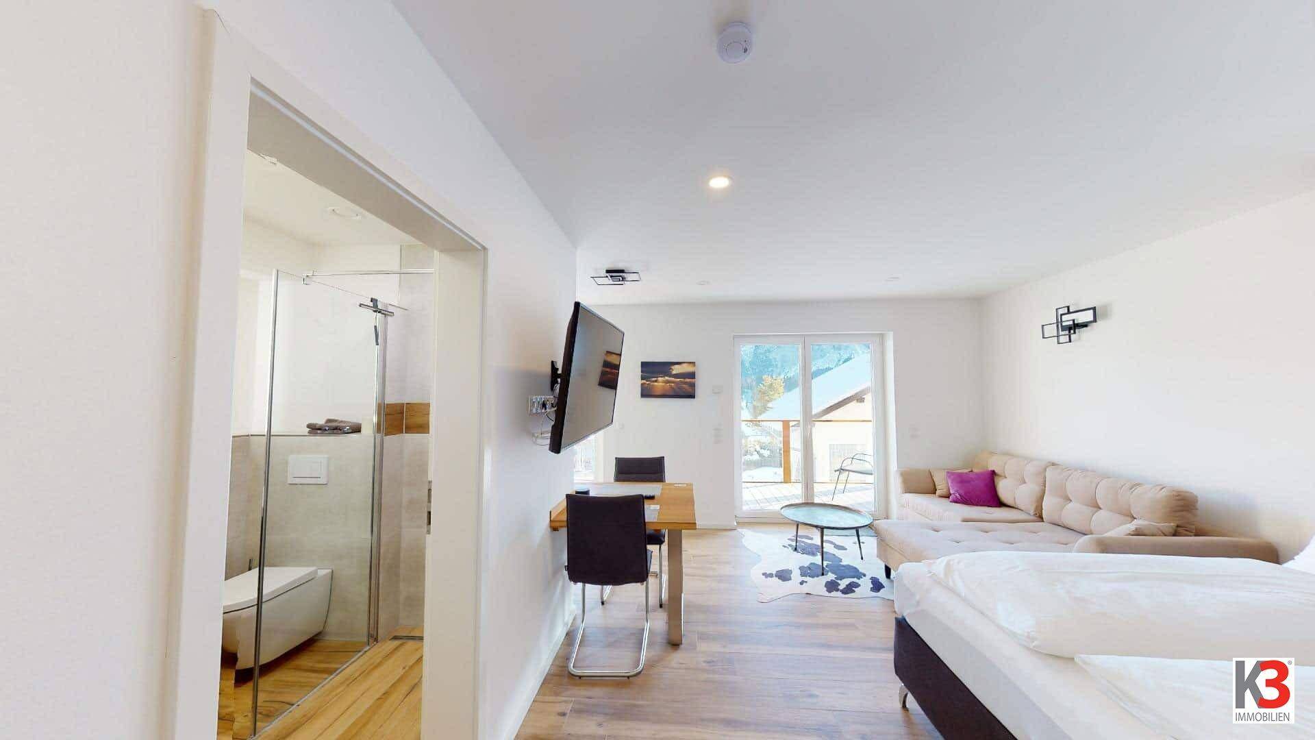 Offener Wohnbereich mit Bett, Sofa, Essplatz und Blick ins moderne Badezimmer.