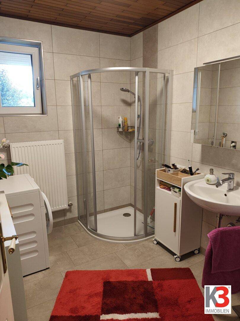 Badezimmer mit Duschkabine, Waschbecken und Fenster, ausgestattet mit einer Waschmaschine.