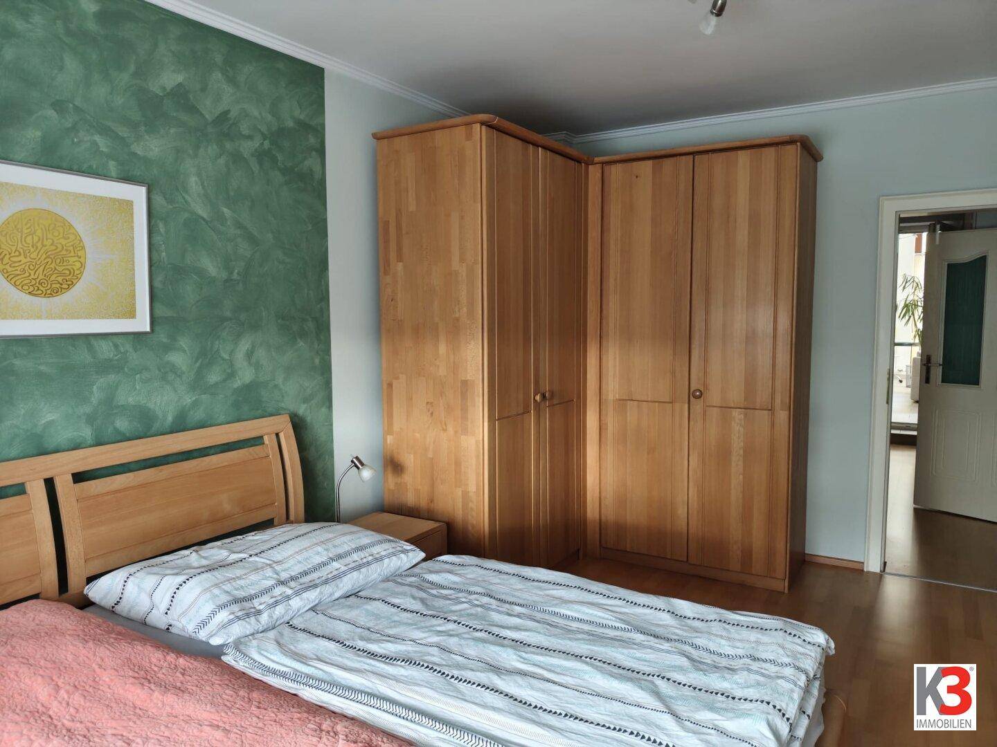 Gemütliches Schlafzimmer mit Holzbett und Eckkleiderschrank, bietet direkten Zugang zu einem anderen Raum.