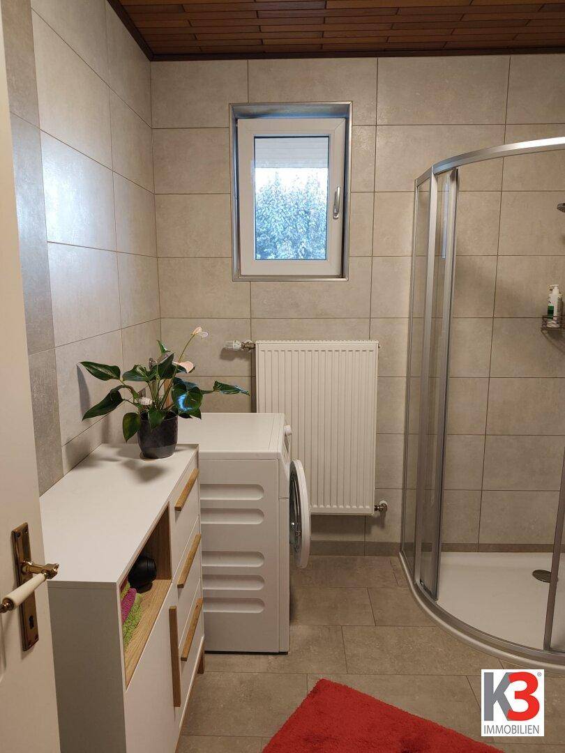 Modernes Badezimmer mit Duschkabine, Fenster und Heizkörper, bietet eine helle und funktionale Einrichtung.