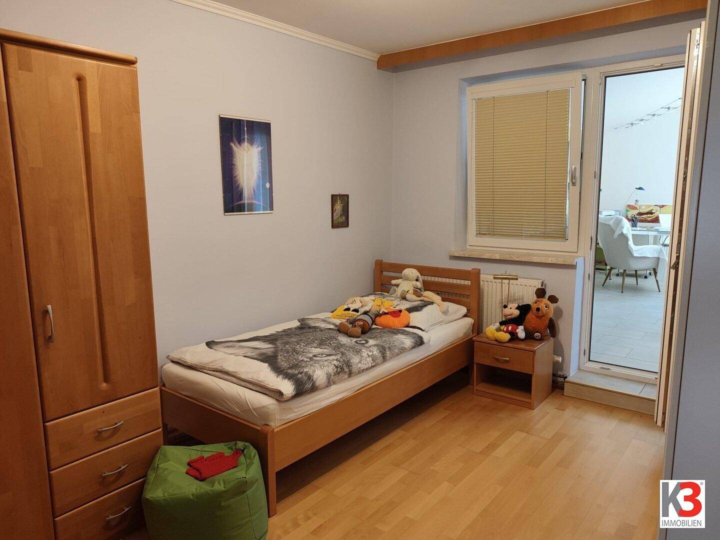 Kinderzimmer mit Einzelbett, Holzschrank und Zugang zu einem hellen Wintergarten.