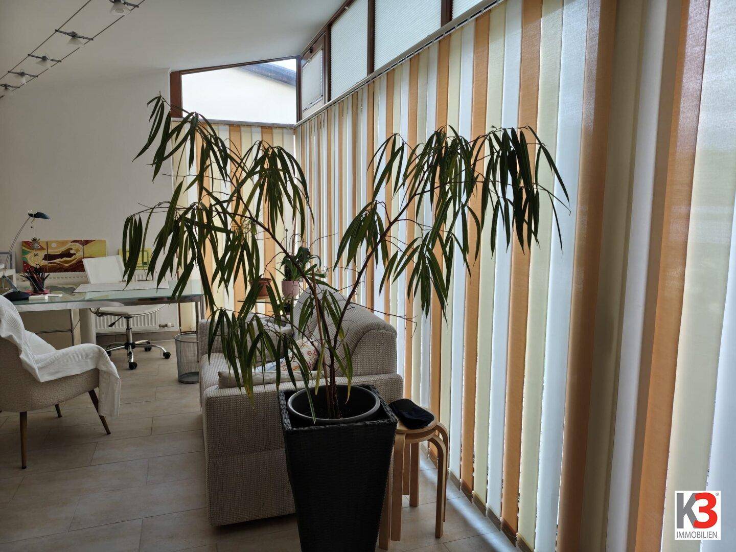 Lichtdurchfluteter Wintergarten mit vertikalen Jalousien und einem großen Fenster, der als Wohnbereich dient.