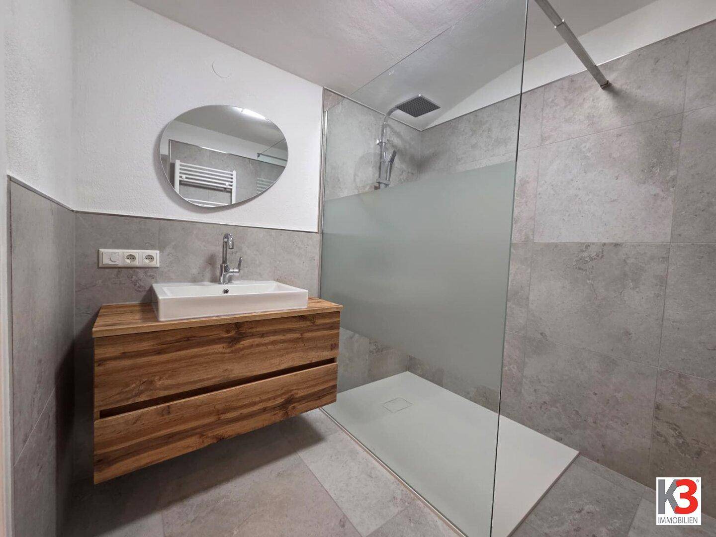 Modernes Badezimmer mit begehbarer Dusche, Holzwaschtisch und grauen Fliesen.