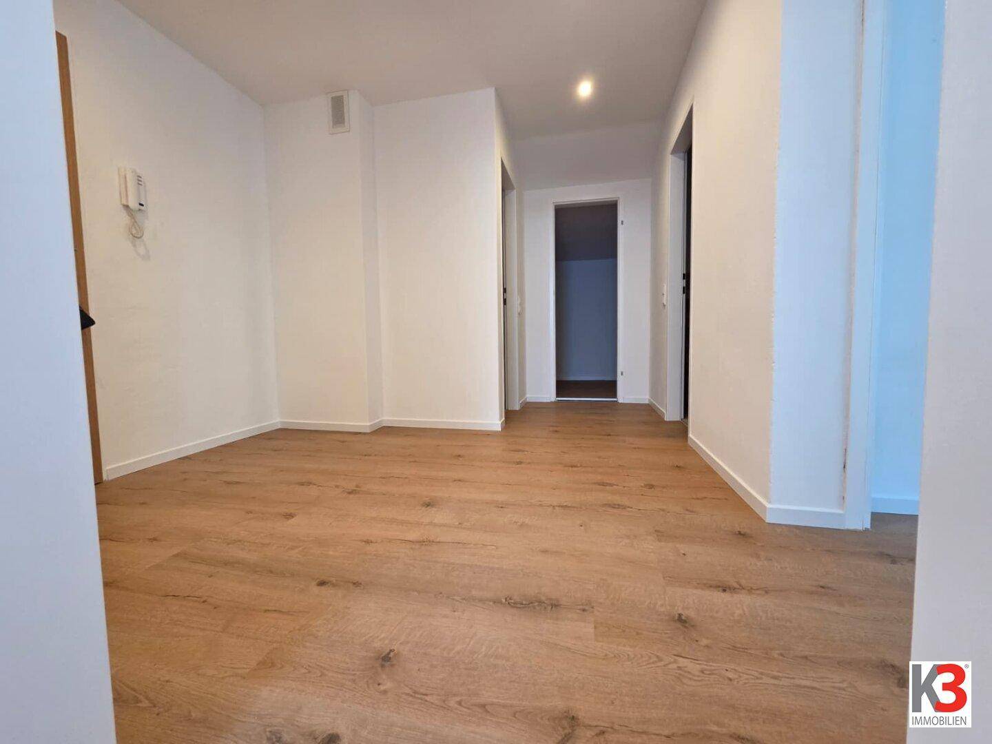 Geräumiger Flur mit hellem Laminatboden und weißen Wänden, der zu weiteren Räumen führt.
