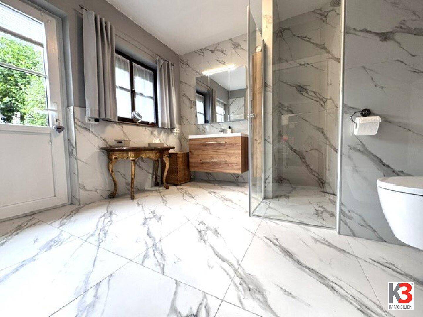 Modernes Badezimmer mit Marmoroptik-Fliesen, begehbarer Dusche und Fenster für natürliches Licht.