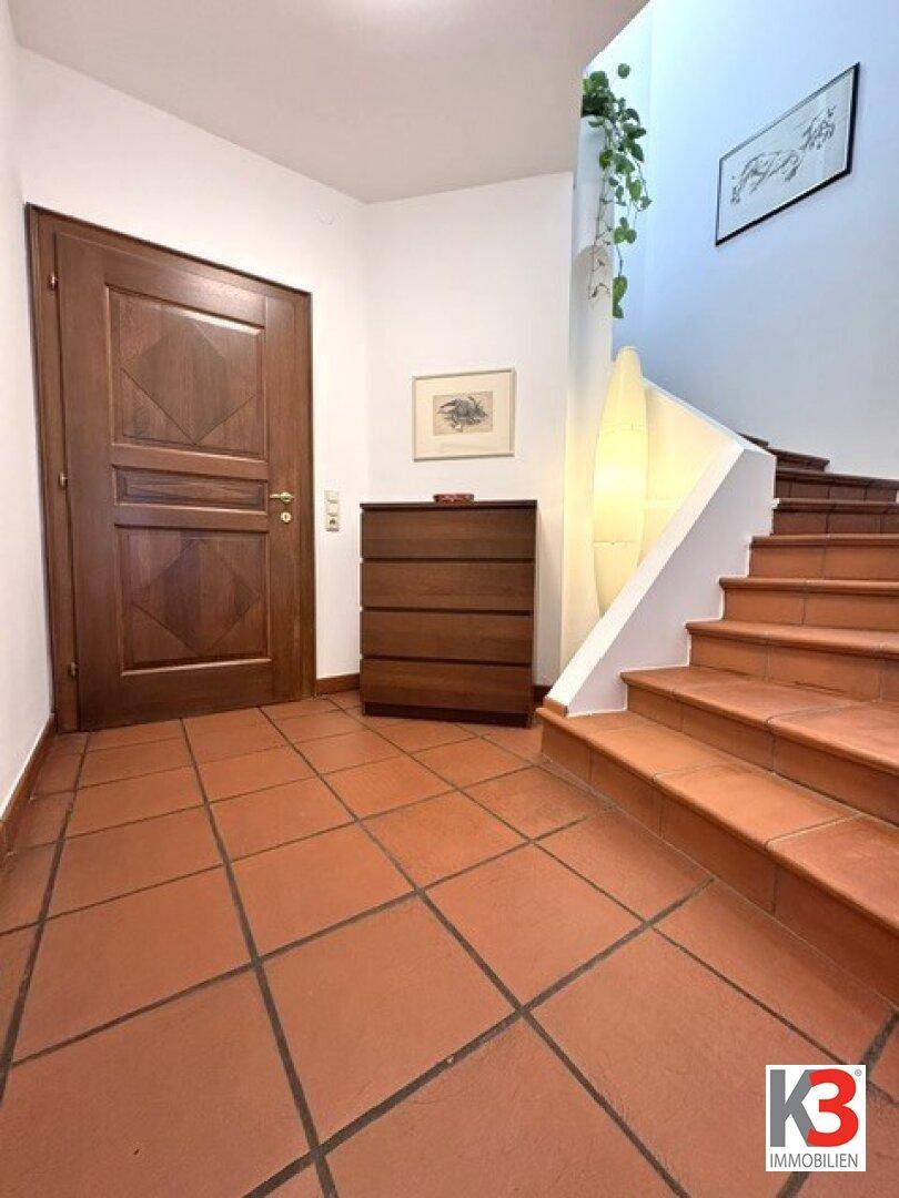 Eingangsbereich mit massiver Holztür, Terrakotta-Fliesenboden und Zugang zur Treppe.
