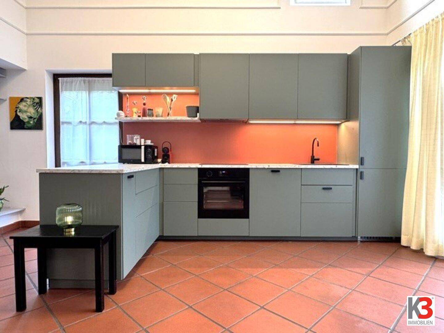 Moderne Küche mit grauen Schränken, orangefarbener Rückwand und Terrakotta-Fliesenboden.