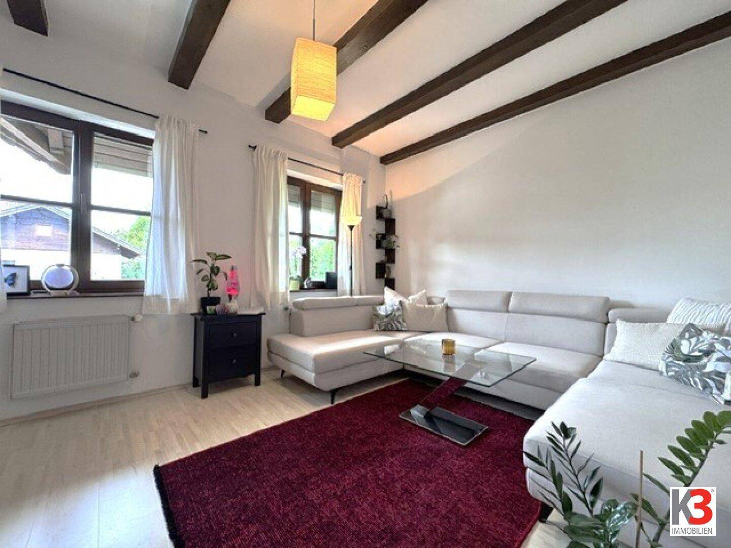 Gemütliches Wohnzimmer mit sichtbaren Holzbalken, großem Sofa und Blick auf die Umgebung.