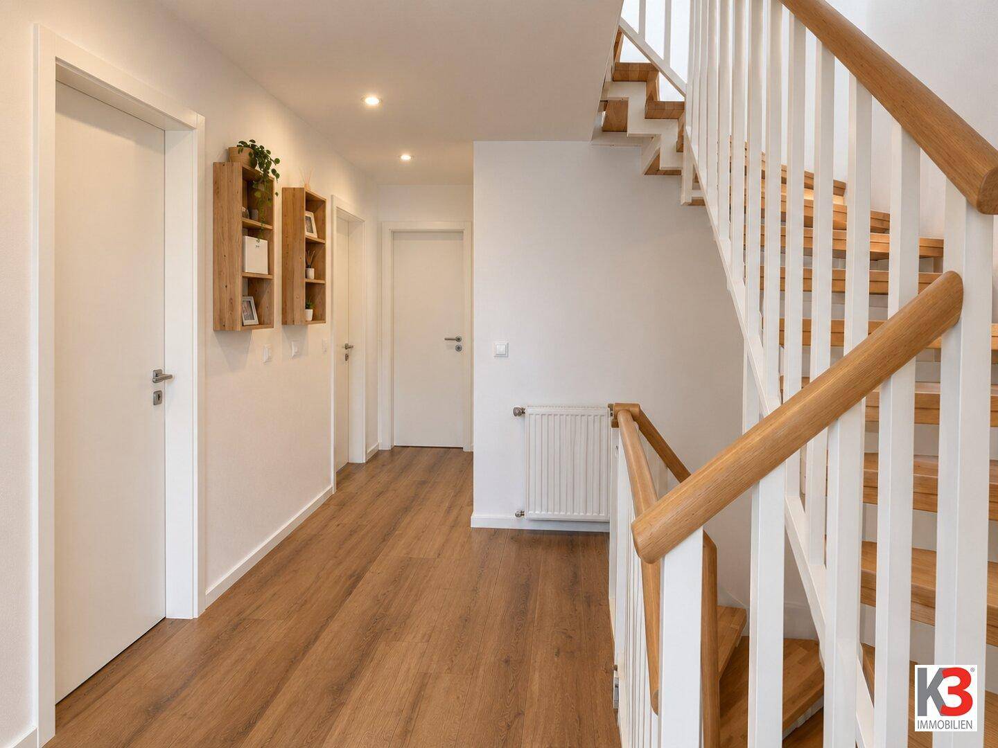 Heller Flur mit Holztreppe, Holzboden und weißen Wänden.