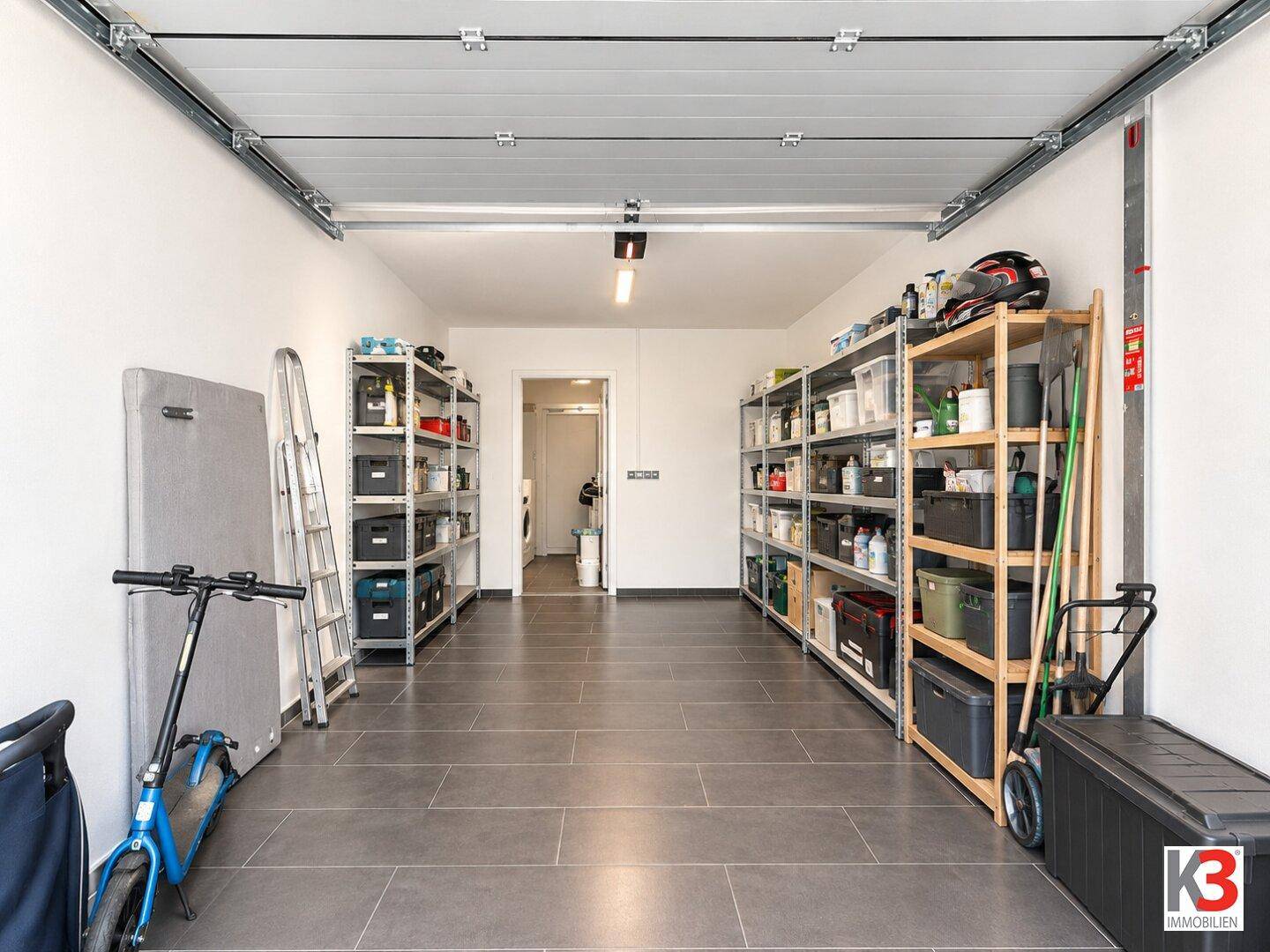 Geräumige Garage mit Fliesenboden, Regalen und viel Stauraum.